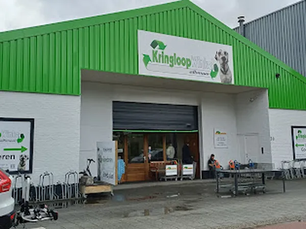 Groene en witte gevel van kringloopwinkel met open rolluik-deur, winkelnaambord bovenop