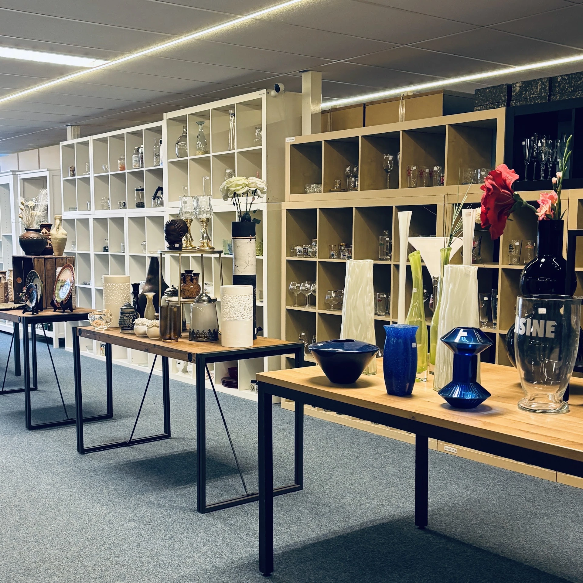 Houten tafels met uitgestalde decoratieve artikelen: vazen, bloemen en accessoires in blauw en rood