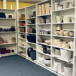 Witte stellingen vol servies, vazen, manden en huishoudartikelen in verschillende kleuren en maten