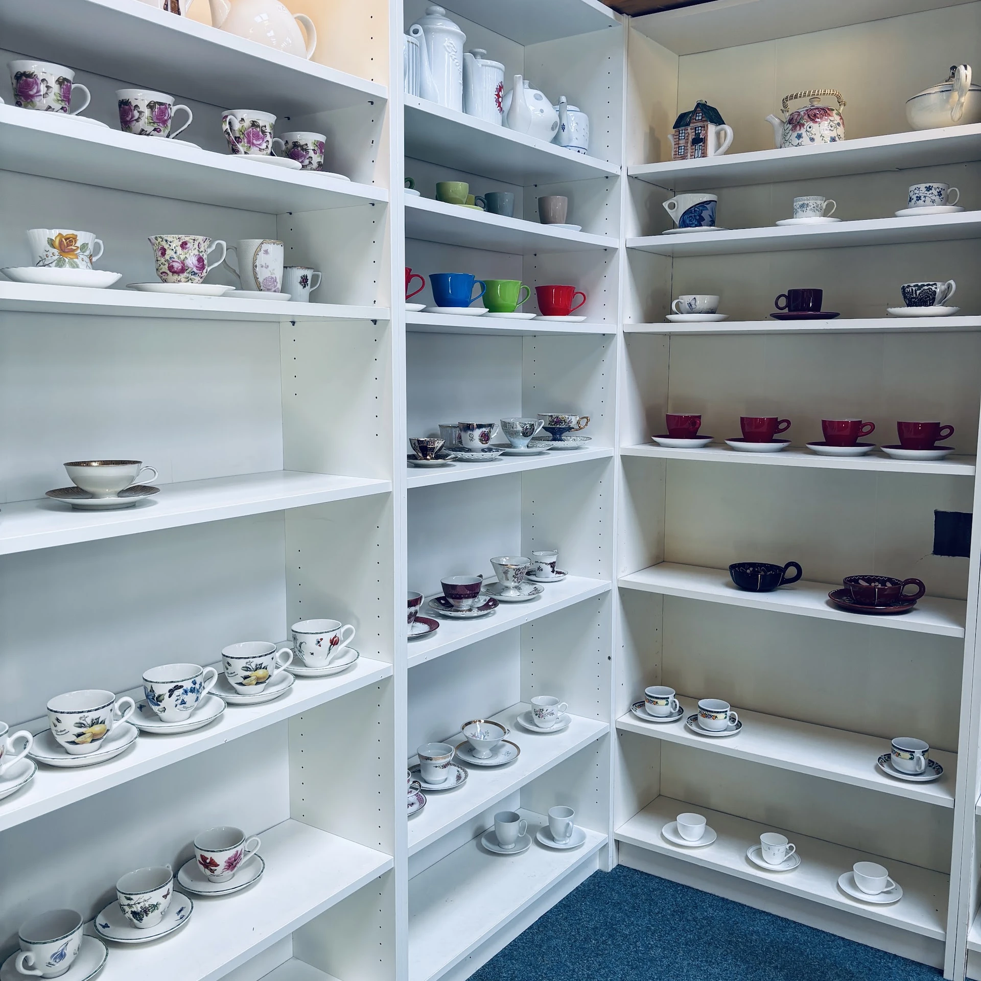 Witte stellingen vol met servies, kopjes en theeglazen in verschillende kleuren en patronen