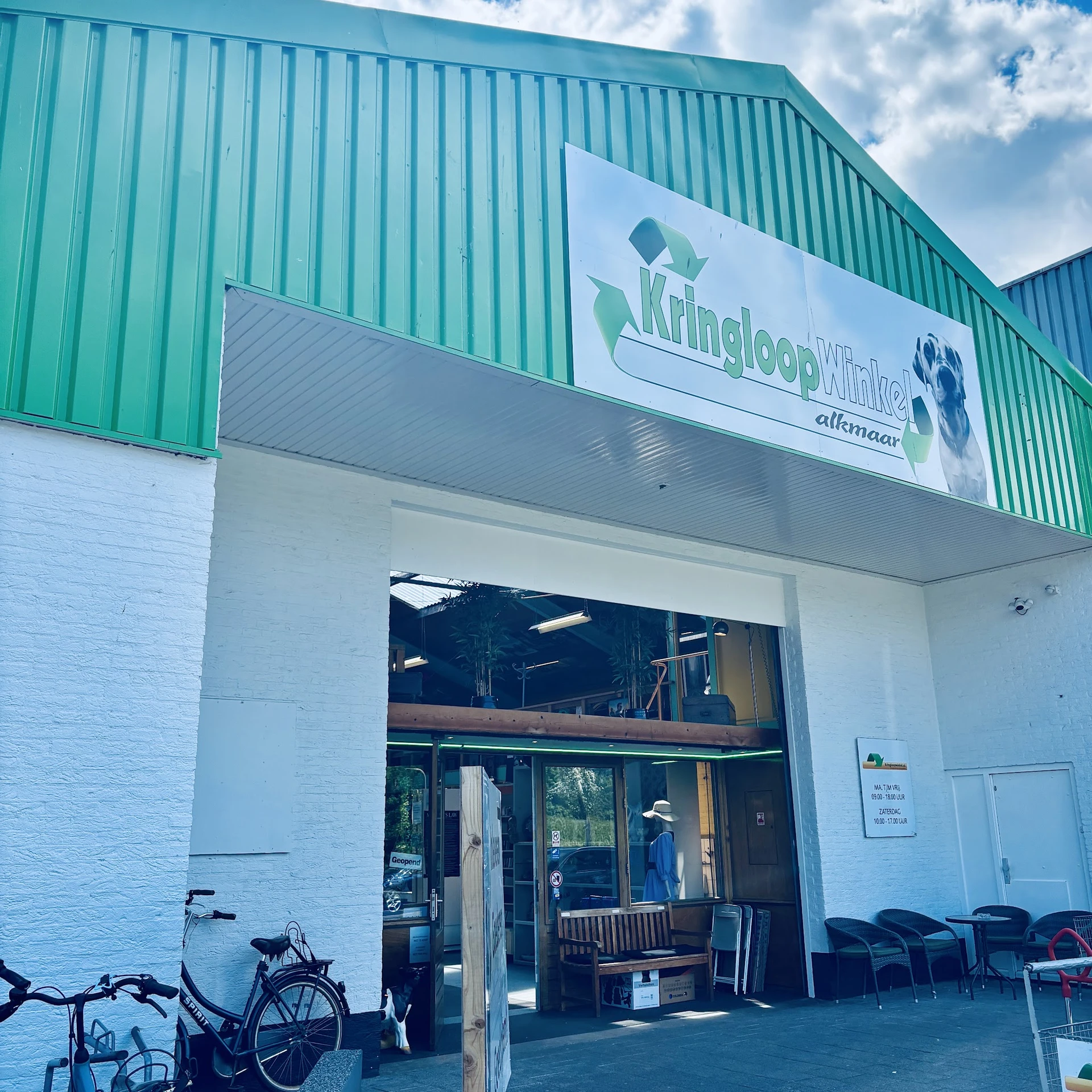 Winkelgevel met groen en wit geschilderd pand, groene golfplaten bovenkant, witte muren en glazen deuren met winkellogo