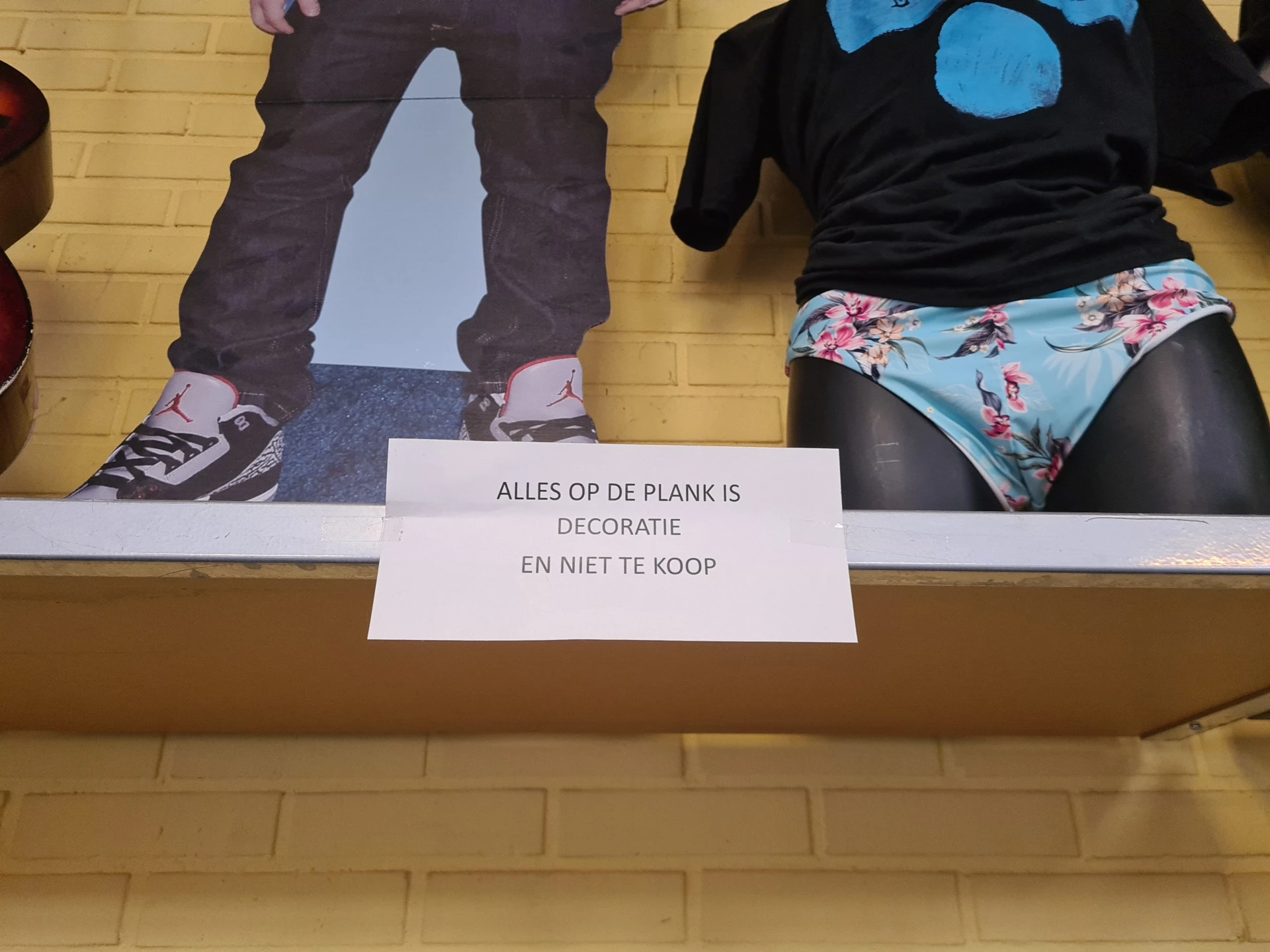 Etalage met tweedehands kleding en accessoires, waarschuwingsbord met Nederlandse tekst