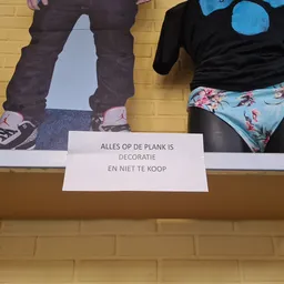 Etalage met tweedehands kleding en accessoires, waarschuwingsbord met Nederlandse tekst