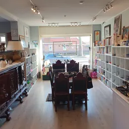 Winkelinterieur met witte stellingen, donkere toonbank en piano in het midden, grote ramen vooraan