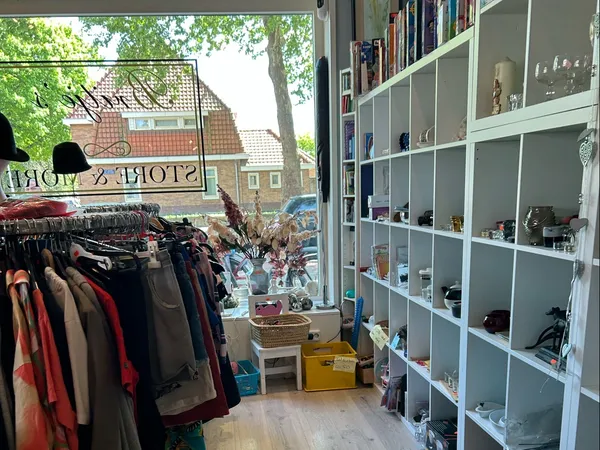 Winkelinterieur met kledingrek links en witte stellingen met diverse spullen rechts, uitzicht op straat door raam