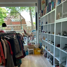 Binnenaanzicht van kringloopwinkel met kledingrek links en wandkasten met diverse artikelen rechts
