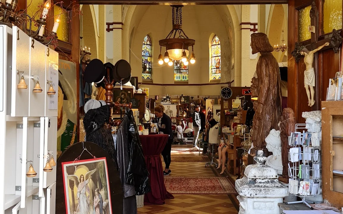 Ruim interieur van kringloopwinkel in voormalig kerkgebouw met stellingen vol spullen en beeldenwerk