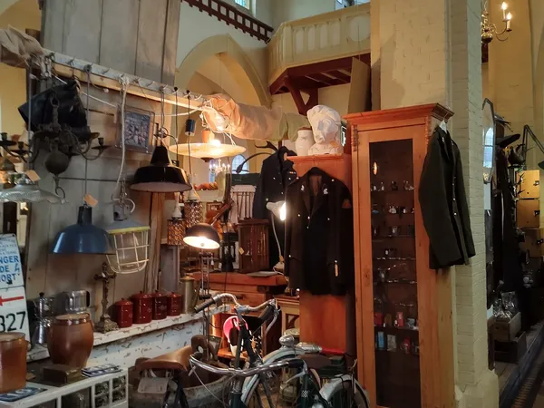 Winkelbinnenruimte met vintage meubels, hangende lampen, kleding aan rekken en diverse tweedehandsartikelen