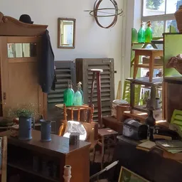 Binnenaanzicht van kringloopwinkel met diverse meubels, glazen flessen, houten stellingen en huishoudelijke spullen