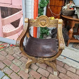 Antieke houten stoel met gesneden gouden armleuningen en bruinleren zitting