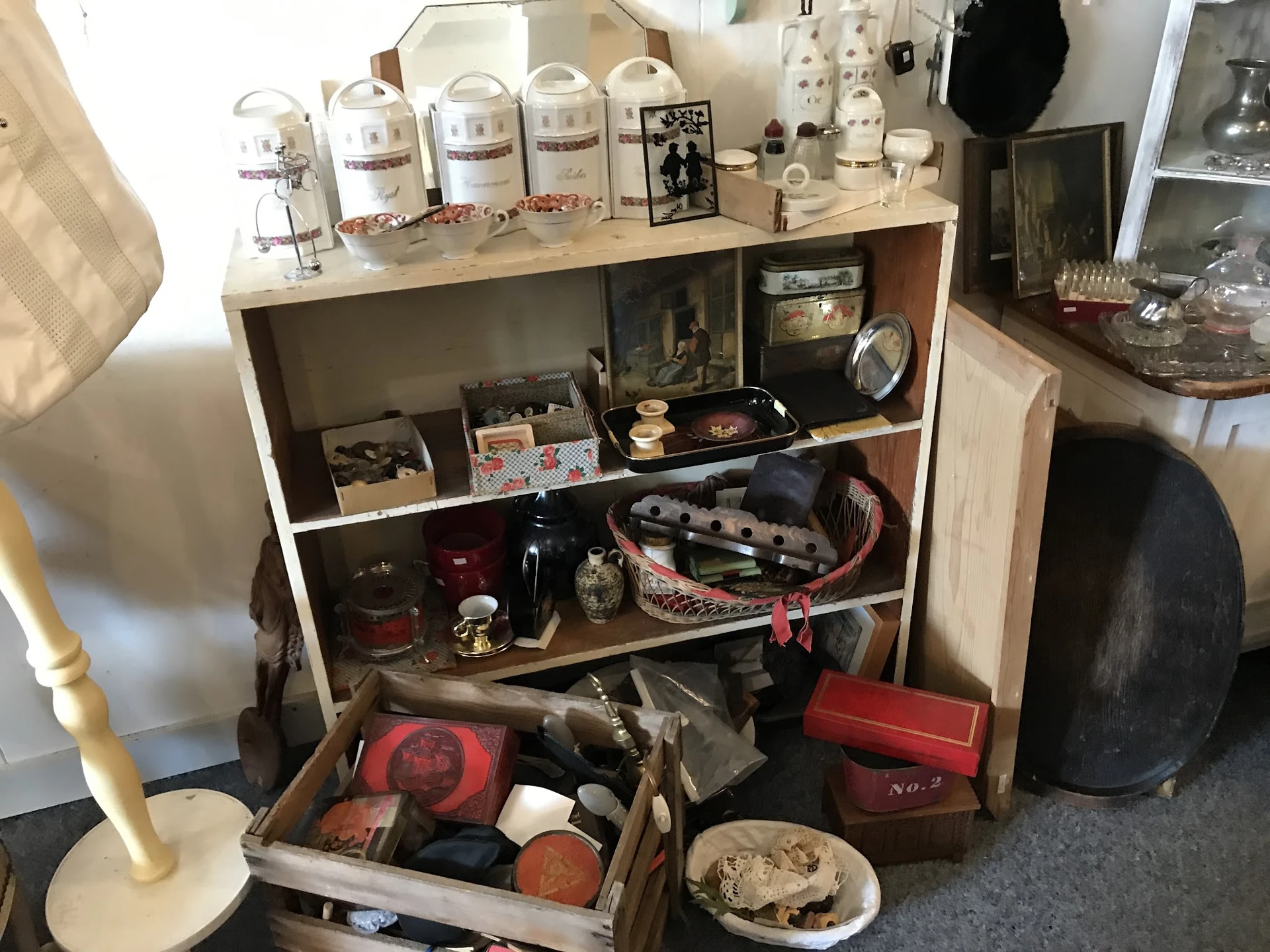 Houten kast met diverse tweedehands spullen: dozen, huishoudartikelen, decoratie en een uitschuiflade met rode en zwarte item