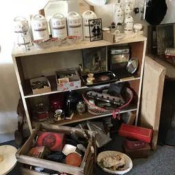 Houten kast met diverse tweedehands spullen: dozen, huishoudartikelen, decoratie en een uitschuiflade met rode en zwarte item