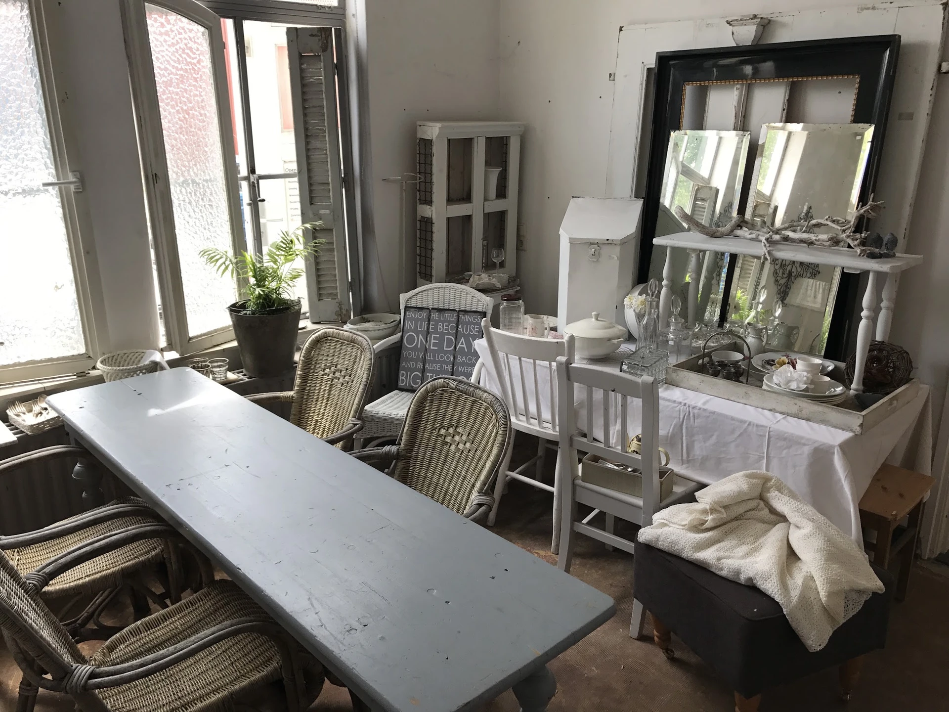 Winkelbinnenruimte met tafels, stoelen, spiegels, planten en diverse huisraad op tafels en stellingen