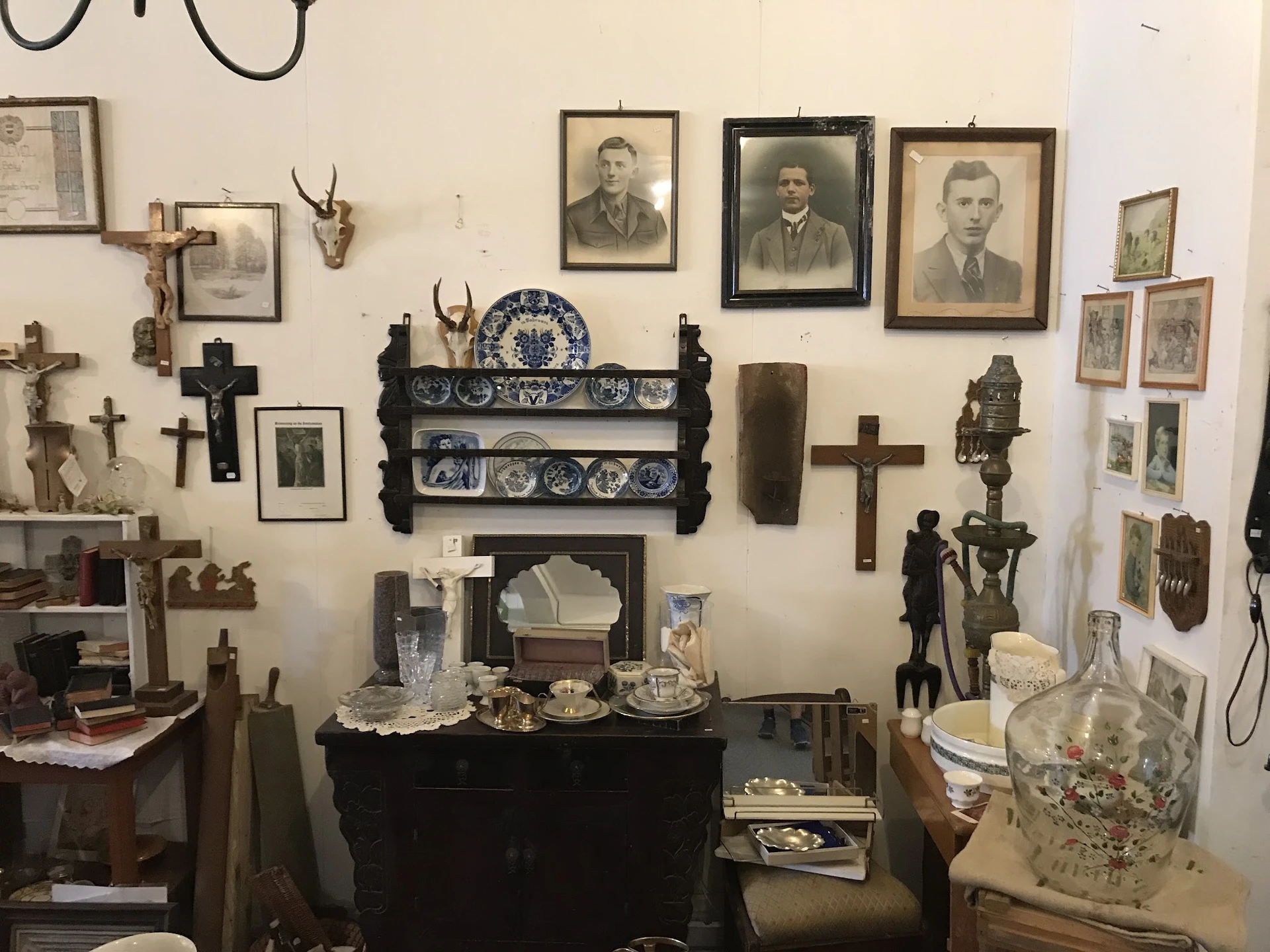 Muurwand met antieke spullen: portretten, kruisen, decoratieve borden, beeldjes en religieuze voorwerpen