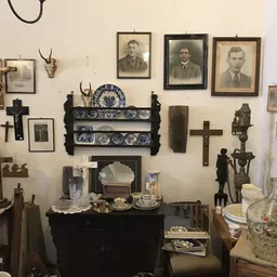 Muurwand met antieke spullen: portretten, kruisen, decoratieve borden, beeldjes en religieuze voorwerpen