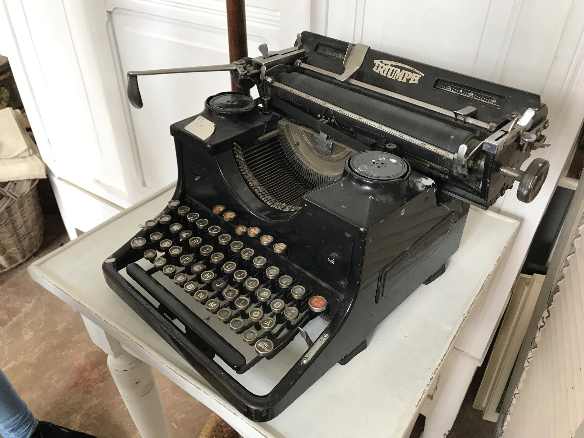 Zwarte vintage typemachine met zichtbaar toetsenbord en papierrol op witte ondergrond