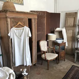 Interieur van een brocantezaak met houten kasten, vintage meubels, een witte jurk op hanger, stoelen en diverse huishoudelijk