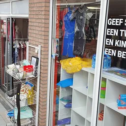 Winkelruit met uitstallingen van kleding, huishoudspullen en speelgoed; witte tekst op raam leesbaar