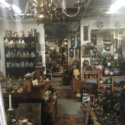 Winkelvloer met diverse vintage en brocante spullen: planken met serviesgoed, hanglampen, klokken, meubels en decoratieve voo