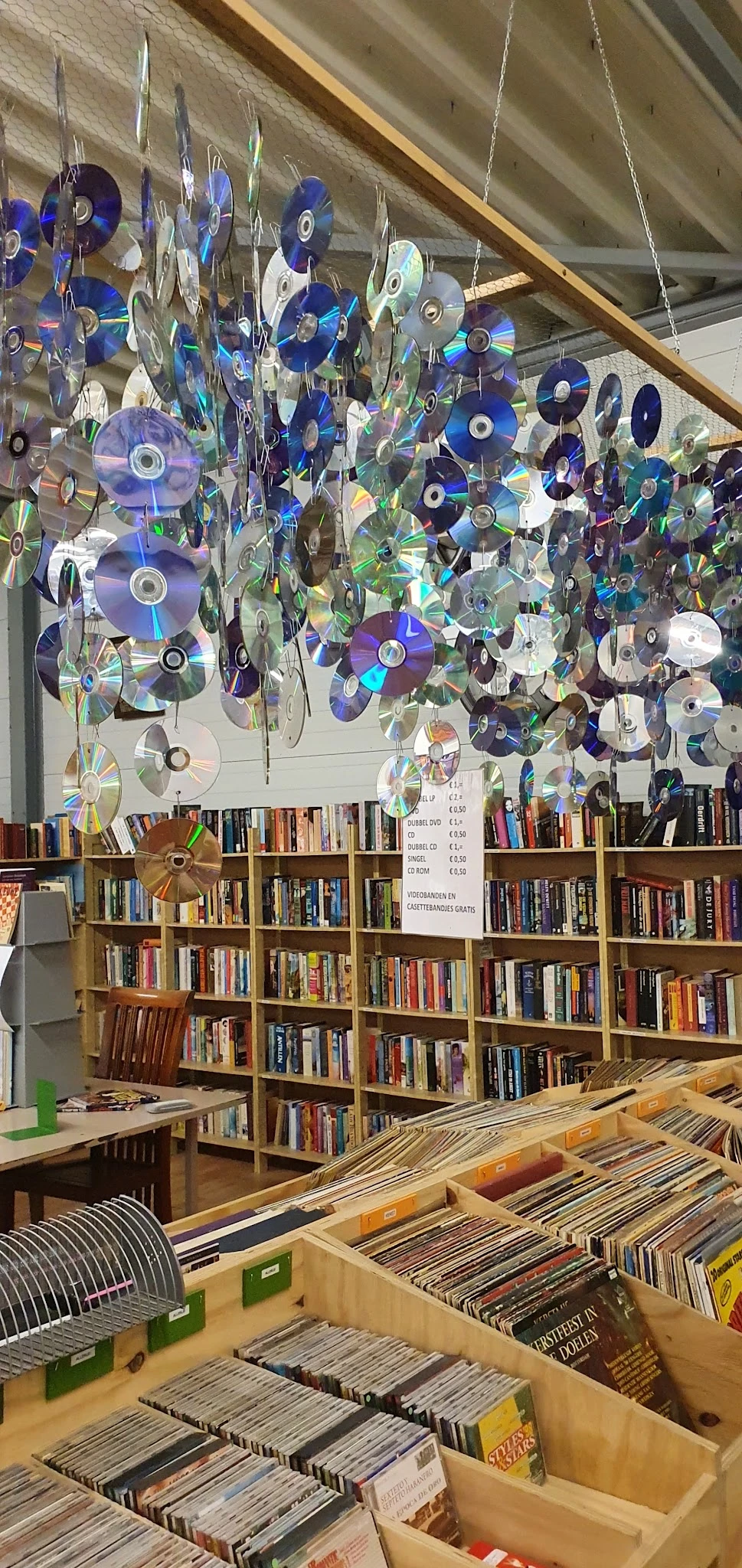 Binnenaanzicht van kringloopwinkel met boekenkasten en decoratieve cd's aan plafond