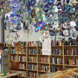 Binnenaanzicht van kringloopwinkel met boekenkasten en decoratieve cd's aan plafond