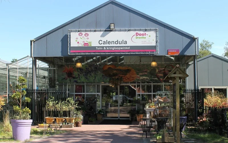 Voorgevel van Calendula tuin- en kringloopwinkel met winkelnaam op bordje, grote ramen, ingang en terras met plantenbakken