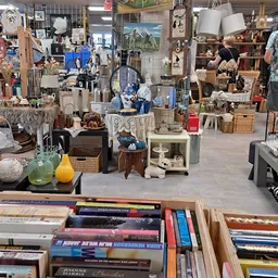 Winkelvloer van kringloopwinkel met boekenrekken op de voorgrond en uiteenlopende spullen en meubels op de achtergrond