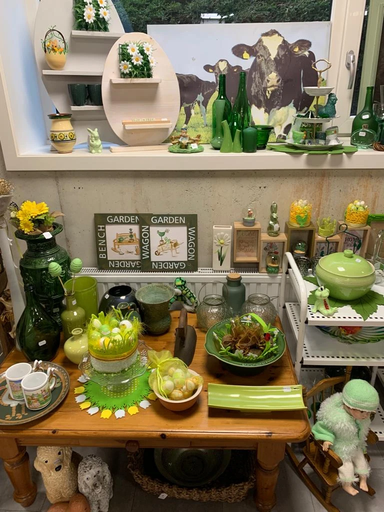Uitgestalde groene en gele decoratieve items, plantenaccesoires en huishoudgoederen op schappen en tafels