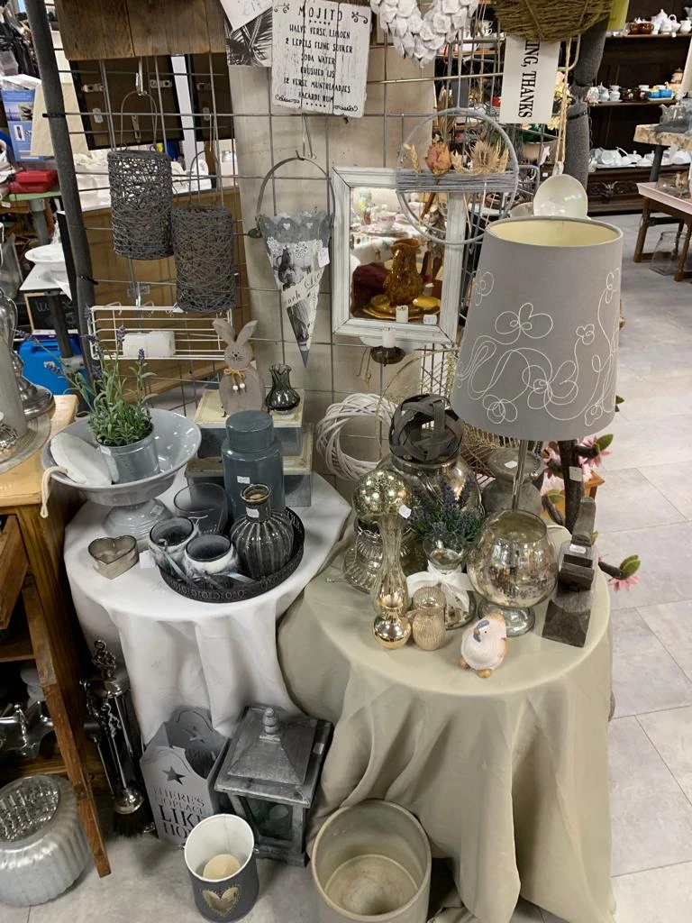 Uitgestalde decoratieve items op tafel: lampen, vazen, bloemen, kandelaars en accessoires