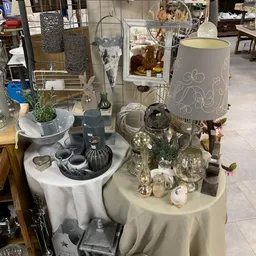 Uitgestalde decoratieve items op tafel: lampen, vazen, bloemen, kandelaars en accessoires