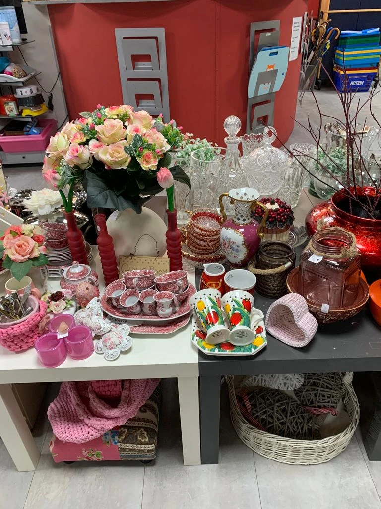 Uitgestalde decoratieve artikelen en serviesgoed in roze en rood, inclusief vazen, kaarsen, glazen en bloemstukken