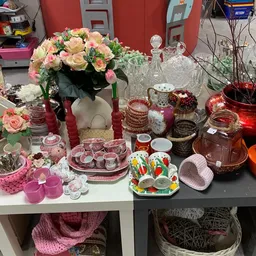 Uitgestalde decoratieve artikelen en serviesgoed in roze en rood, inclusief vazen, kaarsen, glazen en bloemstukken