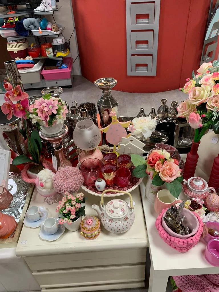 Uitgestalde decoratieve artikelen: vazen, kandelaars, bloemen en servies in roze en gouden tinten