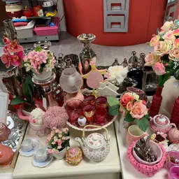 Uitgestalde decoratieve artikelen: vazen, kandelaars, bloemen en servies in roze en gouden tinten