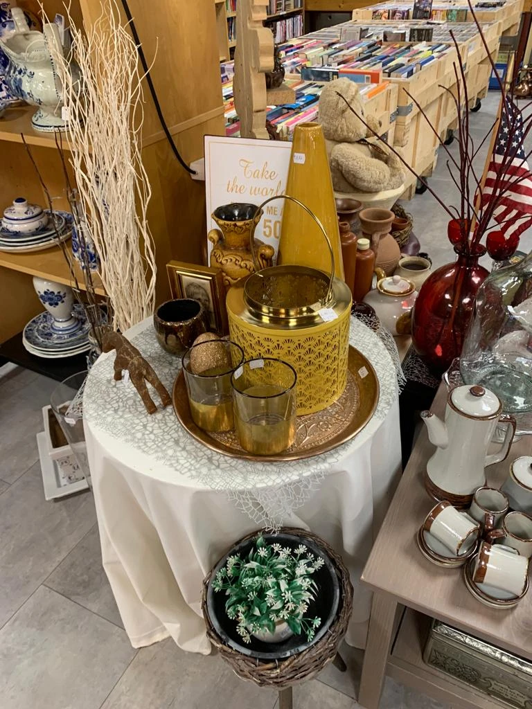 Gouden decoratieve items op een witte tafeltafel, waaronder een kan, glazen en kandelaars