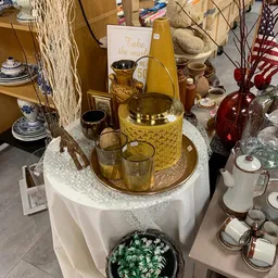 Gouden decoratieve items op een witte tafeltafel, waaronder een kan, glazen en kandelaars