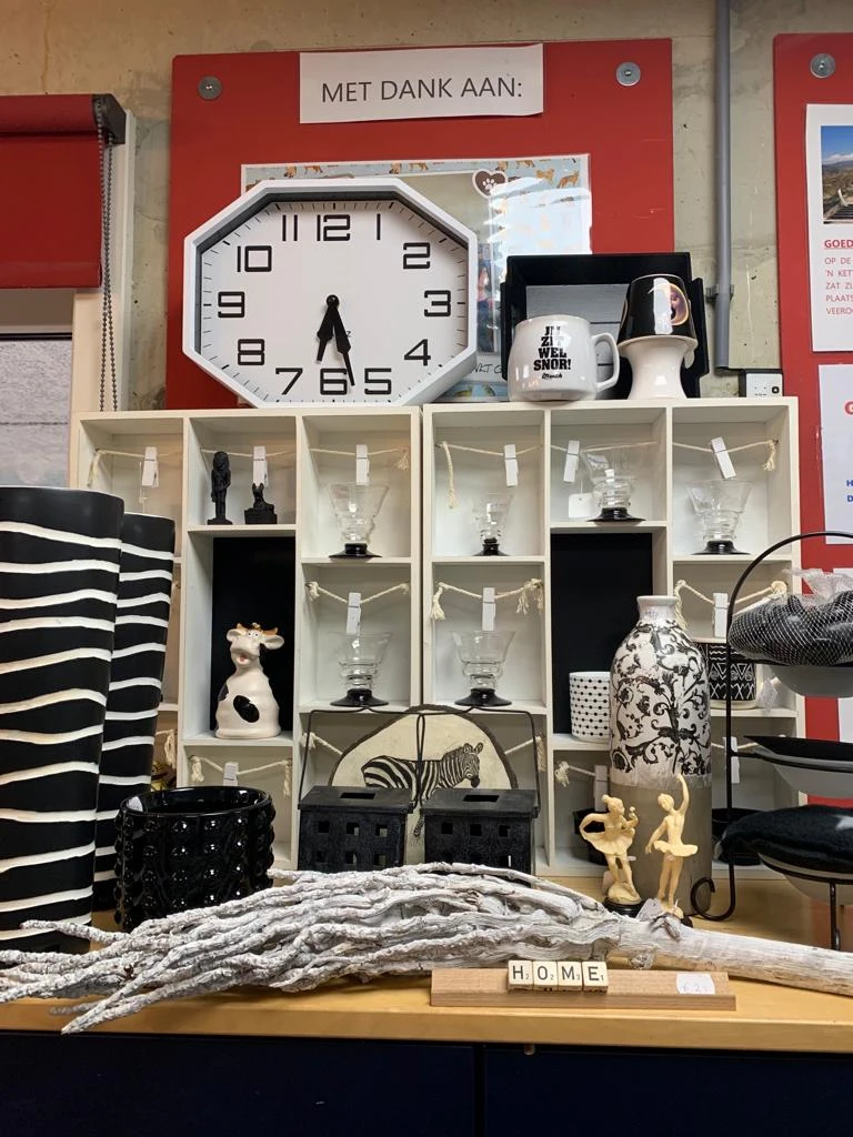 Witte stellingen met decoratieve objecten: beeldjes, vazen, glazen en een klok bovenaan