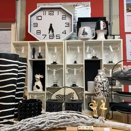 Witte stellingen met decoratieve objecten: beeldjes, vazen, glazen en een klok bovenaan