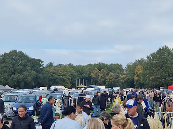 Druk bezocht carbootsale-terrein met veel bezoekers, auto's en uitgestalde spullen onder open lucht