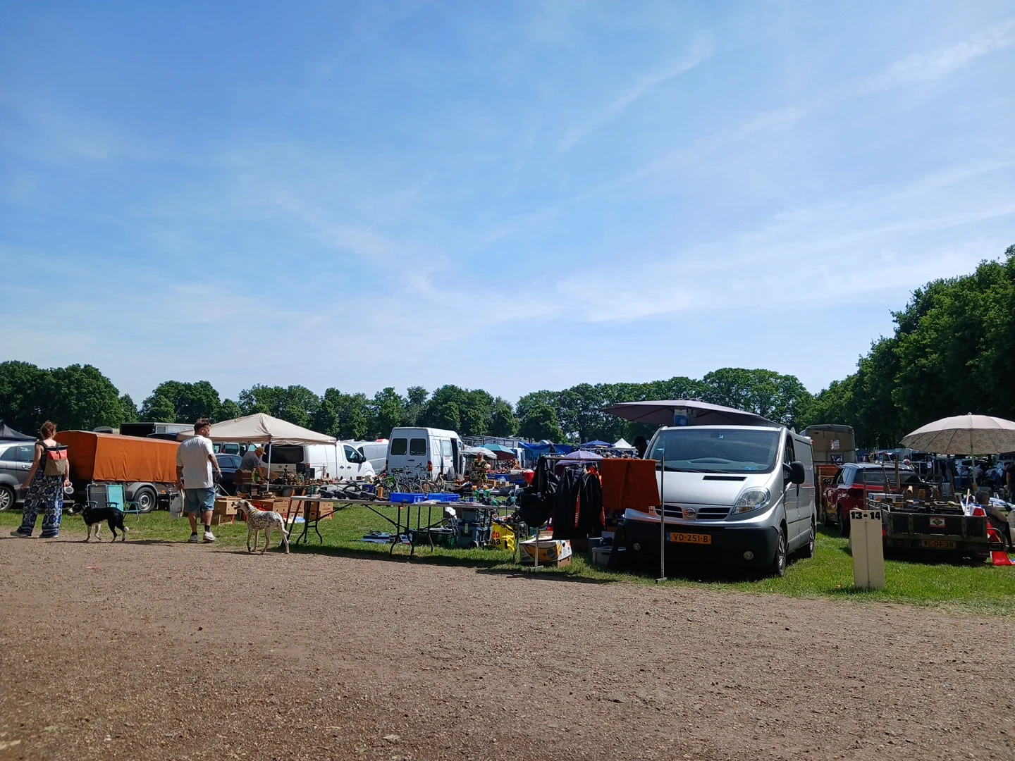 Carbootsale op een grasveld met diverse voertuigen, kraampjes en bezoekers op een zonnige dag