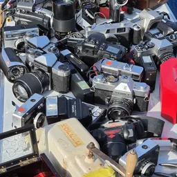 Verzameling tweedehands fotocamera's en filmcamera's uitgestald op een witte ondergrond