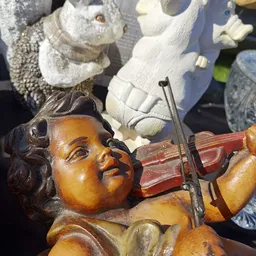 Close-up van een houten beeldje van een engel met viool, met witte decoratieve beelden op de achtergrond