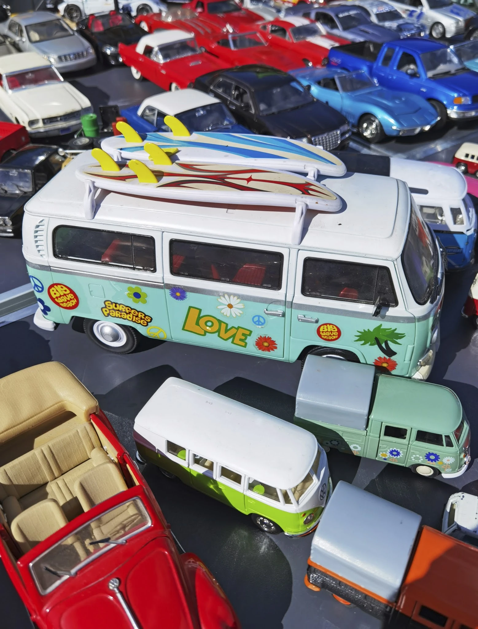 Twee miniatuurbusjes uit een speelgoedcollectie, waarvan één wit-groen met 'LOVE'-opschrift en gele surfboards op het dak