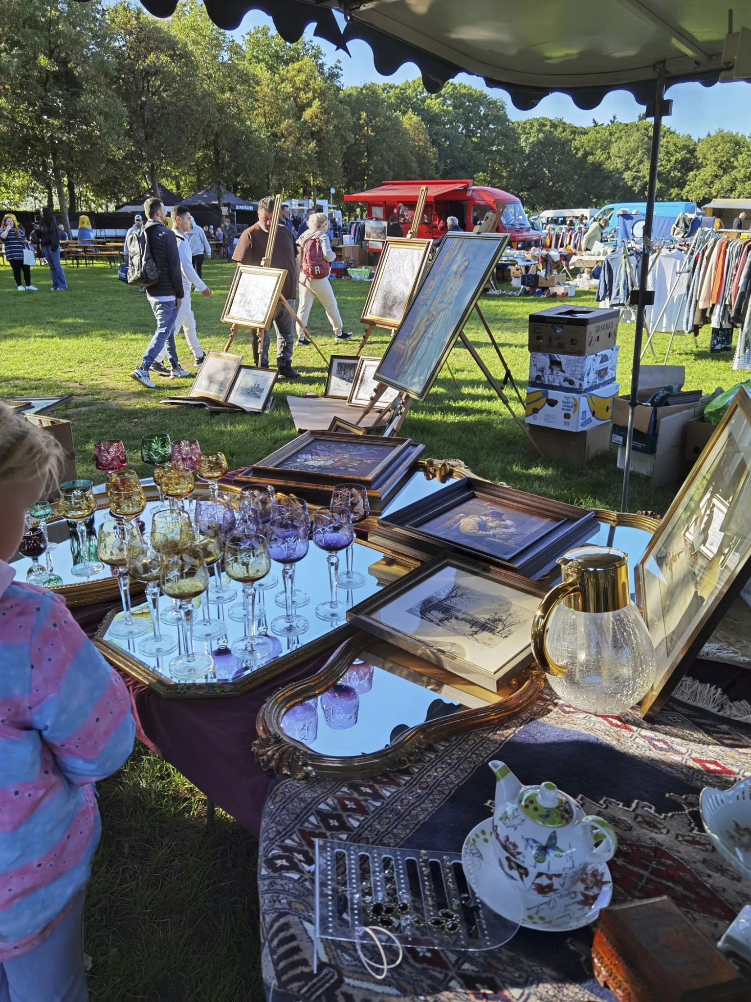 Uitgestalde tweedehandsartikelen op een carbootsale: glazen, kristal, oude prenten en huisraad op een tafel