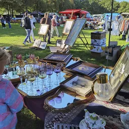 Uitgestalde tweedehandsartikelen op een carbootsale: glazen, kristal, oude prenten en huisraad op een tafel