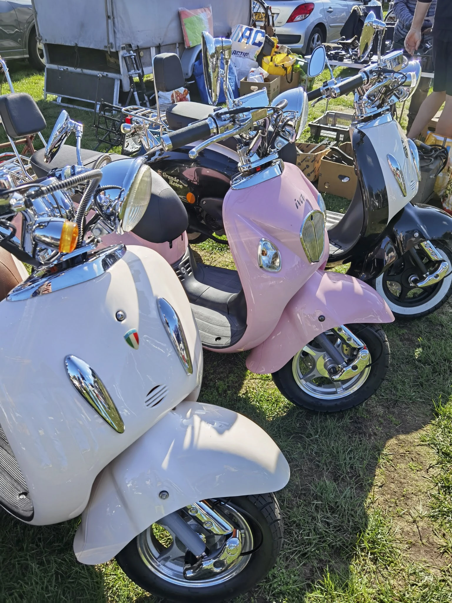 Verzameling vintage scooters in verschillende kleuren, waaronder wit, roze en blauw, geparkeerd op gras