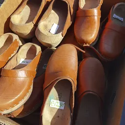 Uitgestalde bruine en beige leren klompen en schoenen op houten vormen