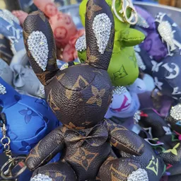 Close-up van een bruine pluchen konijn met glitterdetails en Louis Vuitton-patroon, omgeven door andere gekleurde speelgoedko
