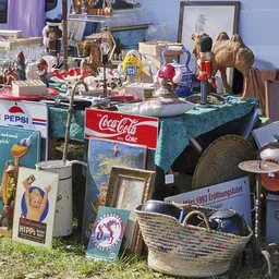 Carbootsale display met vintage items: Pepsi- en Coca-Cola borden, poppen, servies, sieraden en decoratie op blauw kleed