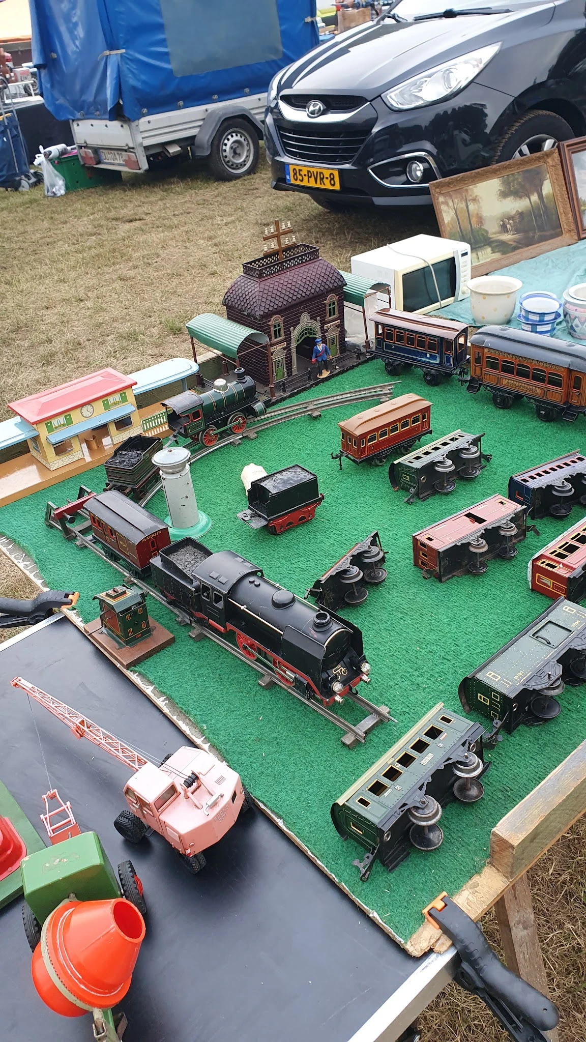 Uitgestalde verzameling miniatuurtreinen en wagons op groen speelbord met stations en accessoires